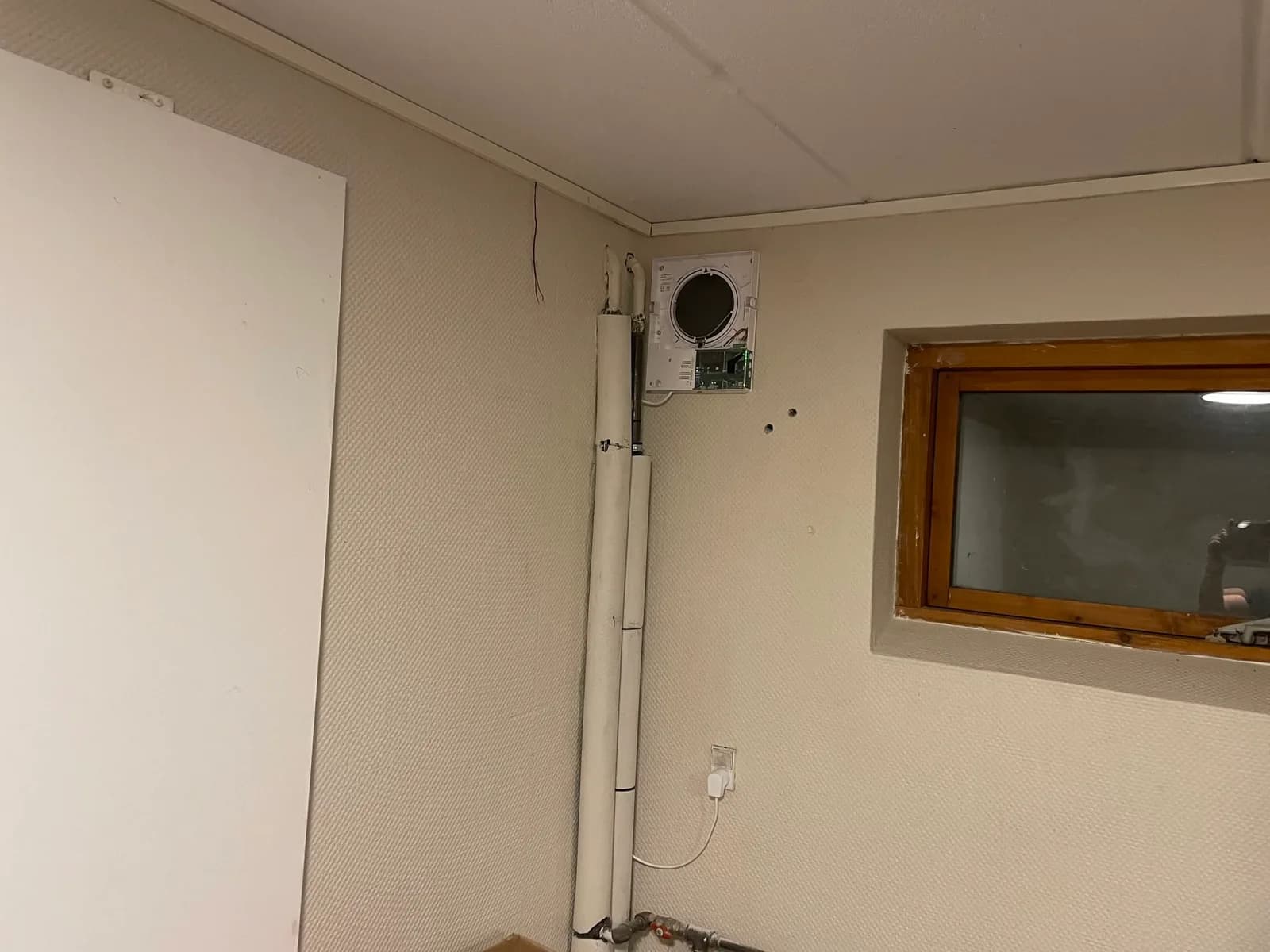 Ventilationsenhed højt på en kældervæg ved et vindue